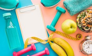 planilha para anotar refeição para musculação ao lado de frutas halteres e outro objetos
